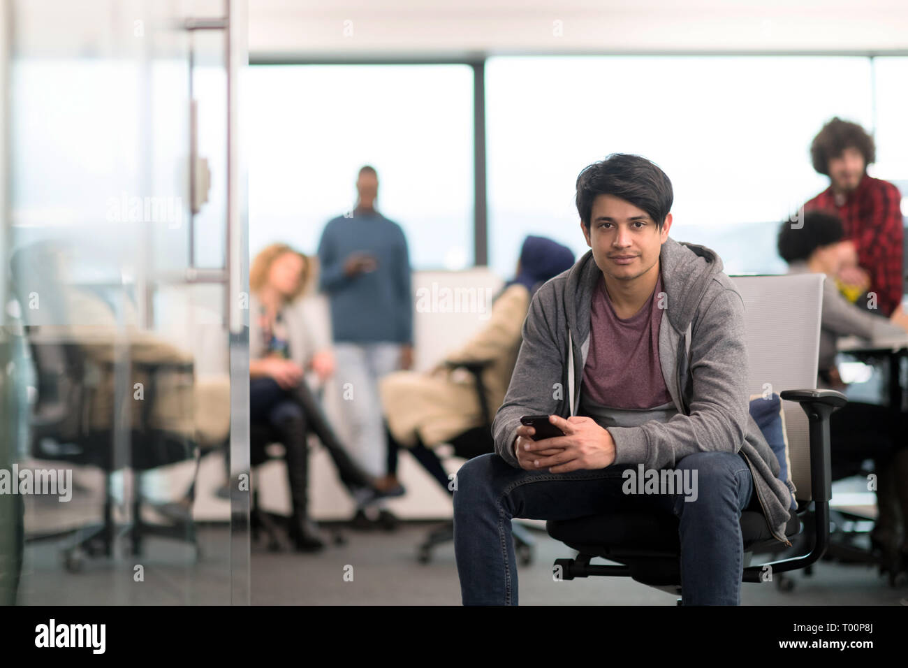 young indian male software developer using mobile phone writing messages while having break at modern creative startup office Stock Photo