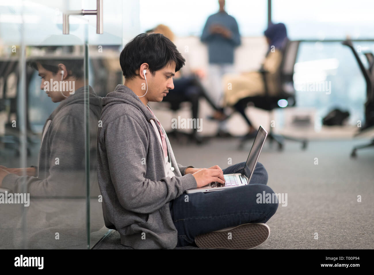 young indian software developer man using laptop computer writing programming code while sitting on the floor at modern creative startup office Stock Photo