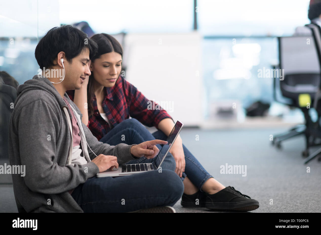 young software developers couple using laptop computer writing programming code while sitting on the floor at modern creative startup office Stock Photo