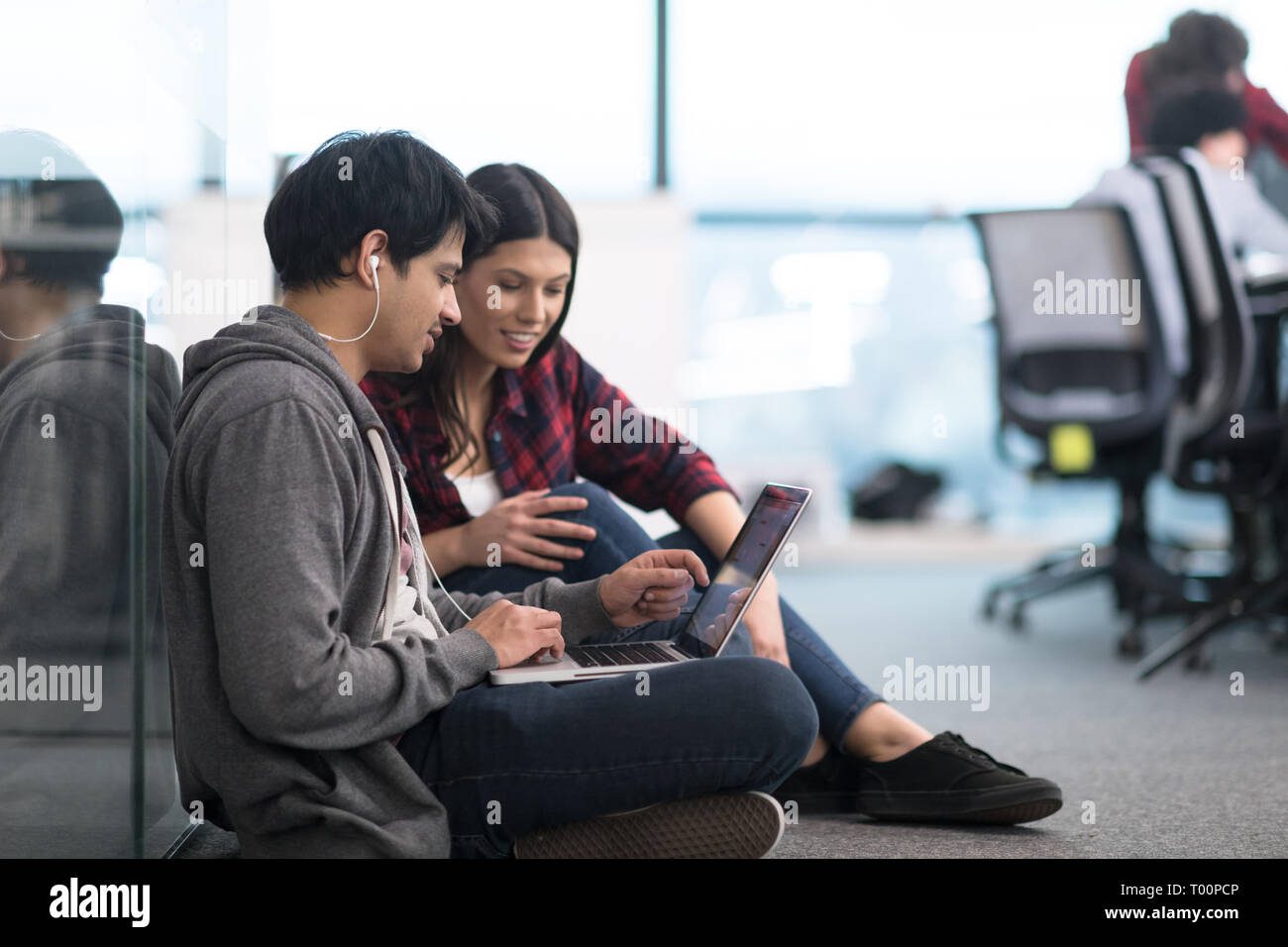 young software developers couple using laptop computer writing programming code while sitting on the floor at modern creative startup office Stock Photo