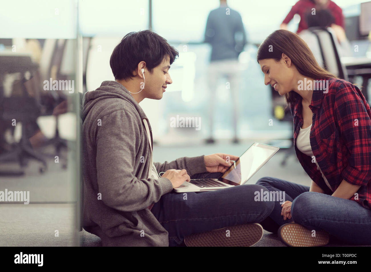 young software developers couple using laptop computer writing programming code while sitting on the floor at modern creative startup office Stock Photo
