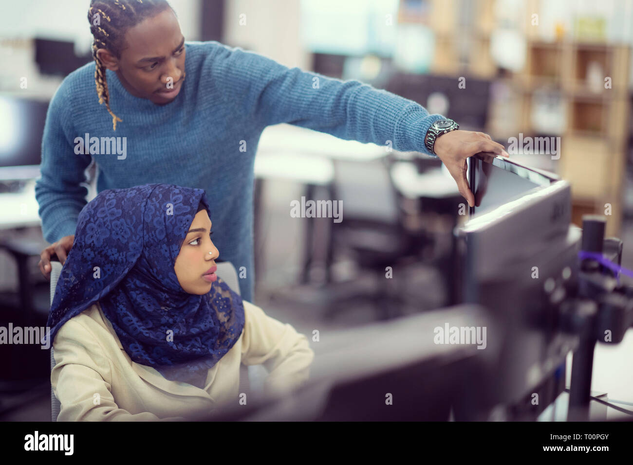 black muslim female software developer working together with her african american male colleague using computer while writing programming code at mode Stock Photo