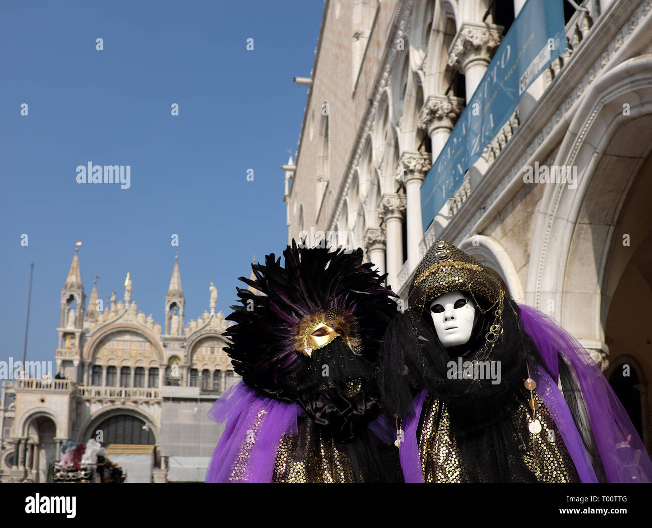 Couple dressed in traditional mask and costume for Venice Carnival standing in Piazza San Marco in front of Saint Mark's Basilica, Venice, Veneto, Ita Stock Photo
