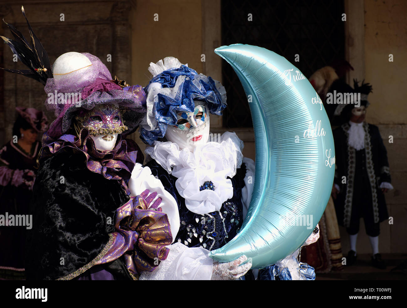 Woman dressed in traditional costume for Venice Carnival holding moon balloon standing at Doge’s Palace, Piazza San Marco, Venice, Veneto, Italy Stock Photo