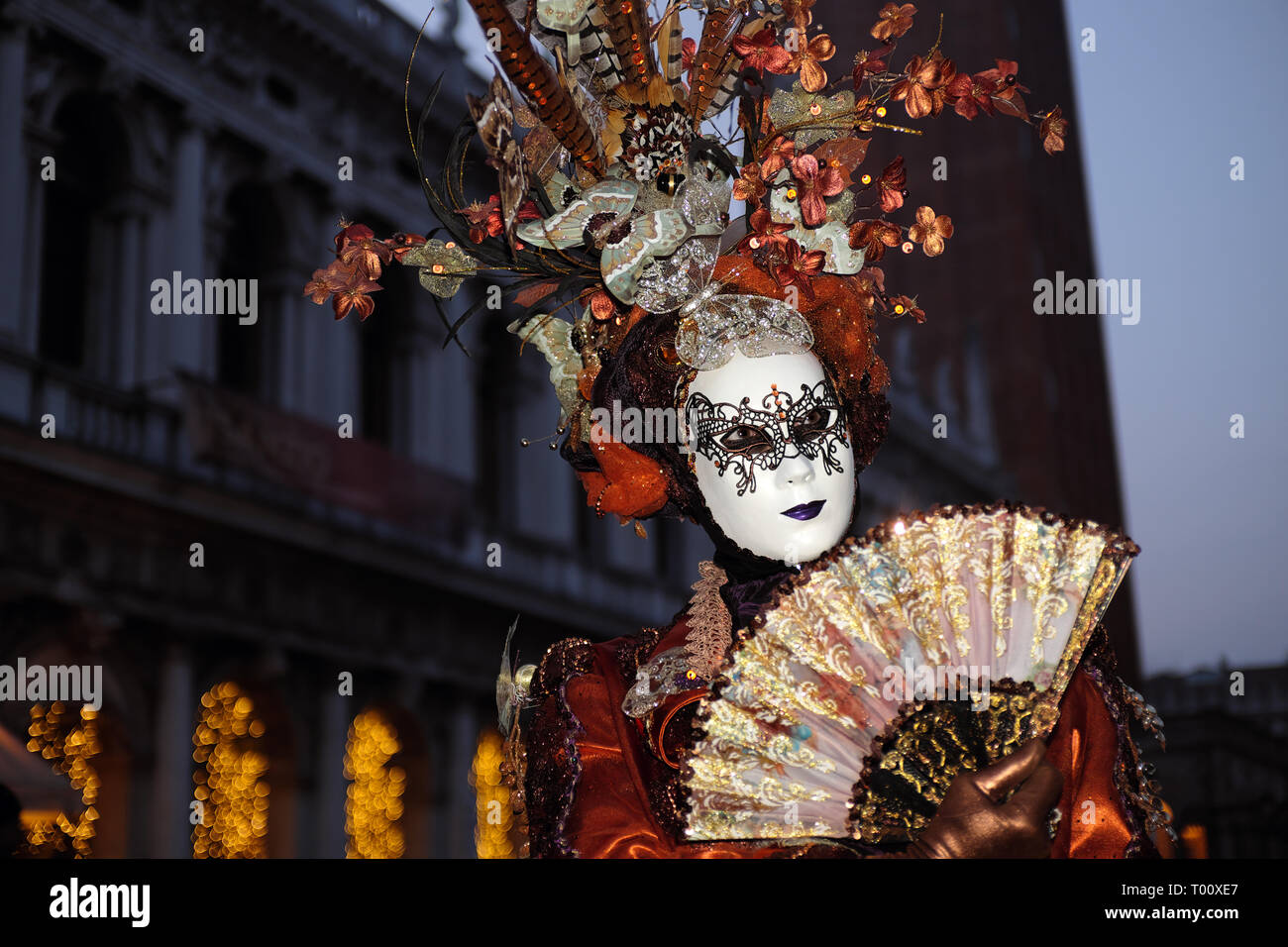 Woman dressed in traditional mask and costume for Venice Carnival standing in Piazza San Marco in front of Saint Mark's Basilica, Venice, Veneto, Ital Stock Photo
