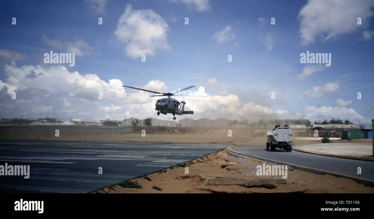 29th October 1993 A U.S. Army Sikorsky UH-60 Black Hawk helicopter takes off from UNOSOM HQ in Mogadishu, Somalia. A Zimbabwe National Army Crocodile TCV drives past. Stock Photo