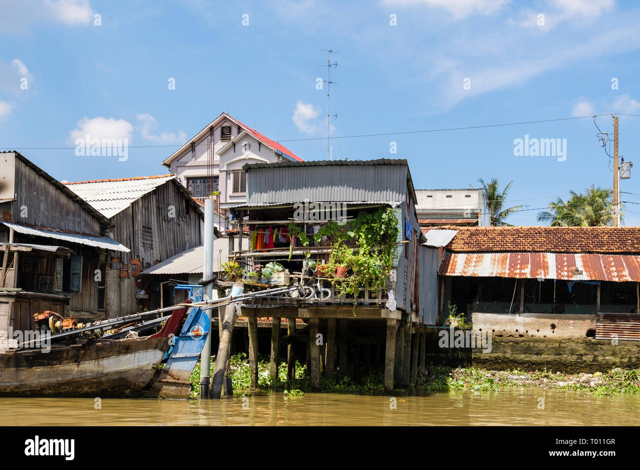 Typical Vietnamese tin shack stilt houses on riverside of Co Chien River in Mekong Delta. Cai Be, Tien Giang Province, Vietnam, Asia Stock Photo