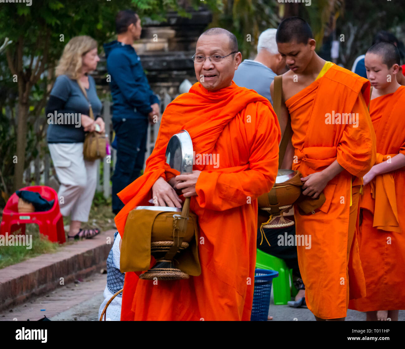 Buddhist monks in orange robes queue for morning alms giving ceremony