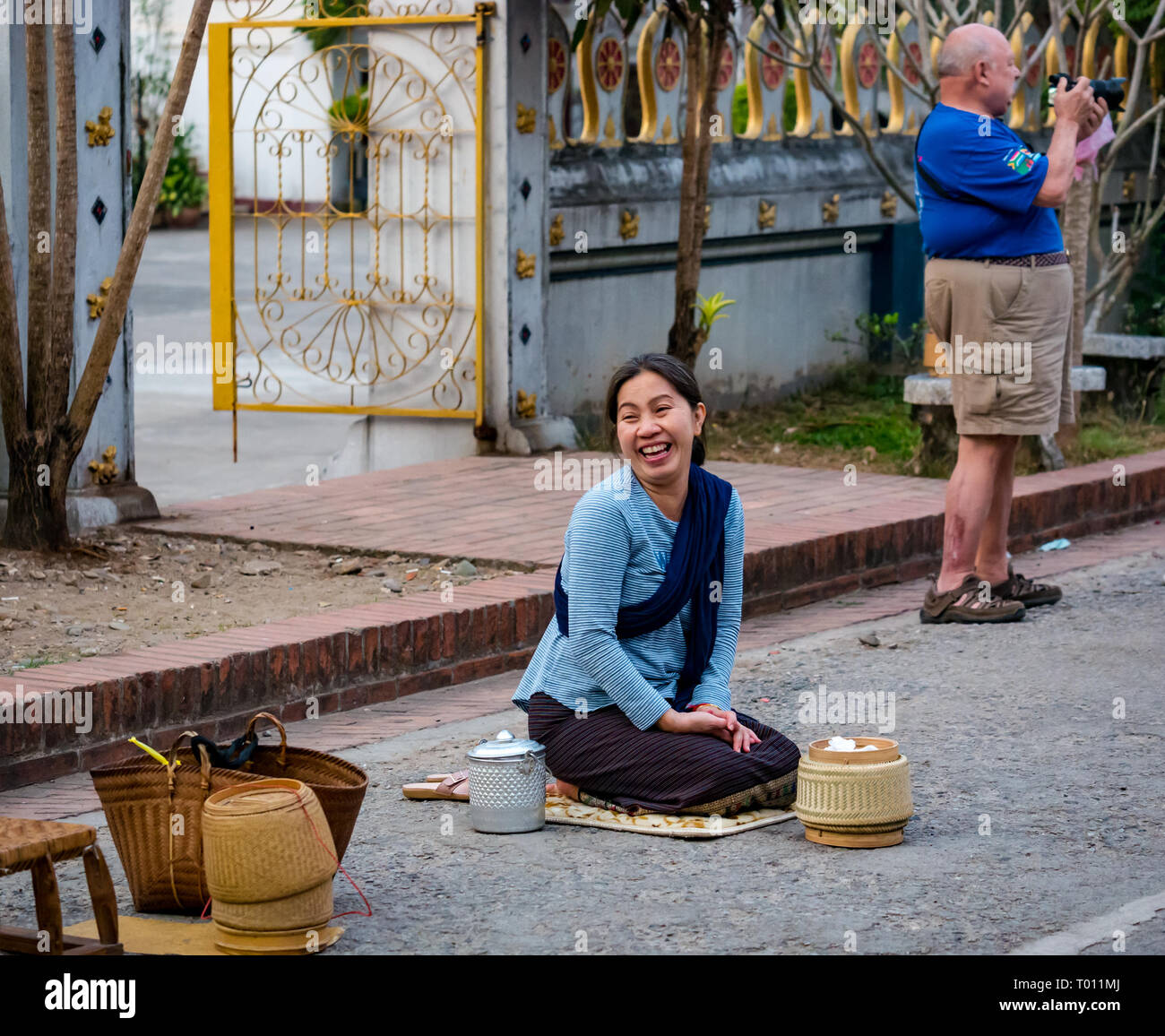 Woman waiting to give rice in morning alms giving ceremony to Buddhist monks with fat tourist man, Luang Prabang, Laos Stock Photo