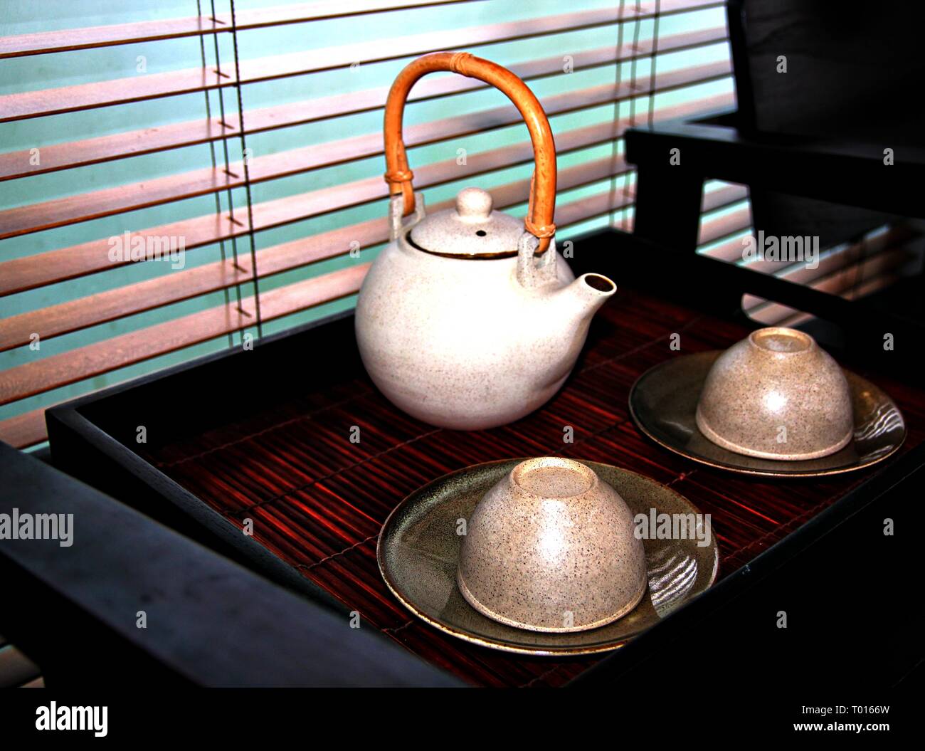 A rustic teapot with rattan handle with matching cup and saucers Stock