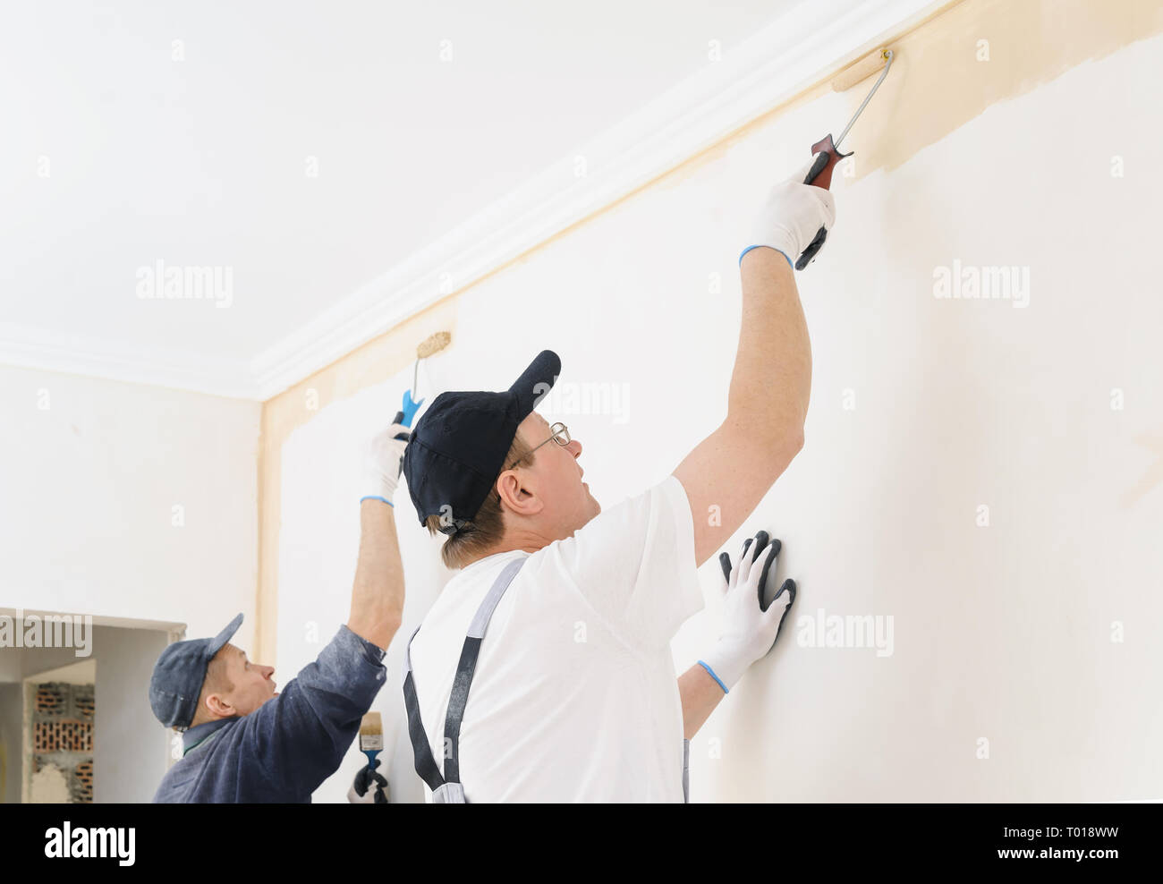 Two workers paint a wall in the room using rollers. Stock Photo