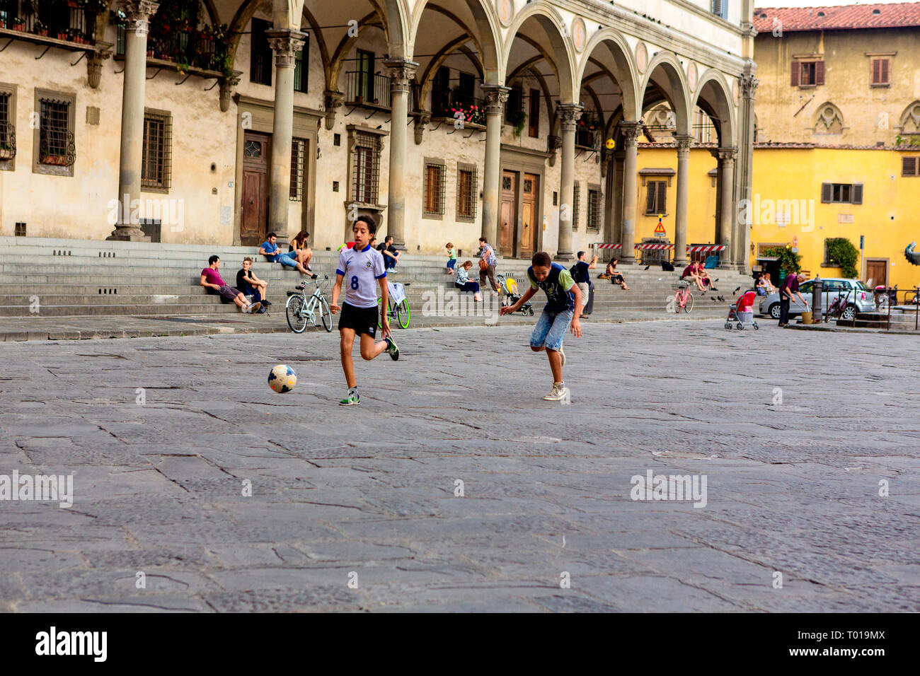 Teenaged boys kick a socerball around the Piazza della Santissima Annunziata, in Florence, in the region of Tuscany, Italy. Stock Photo