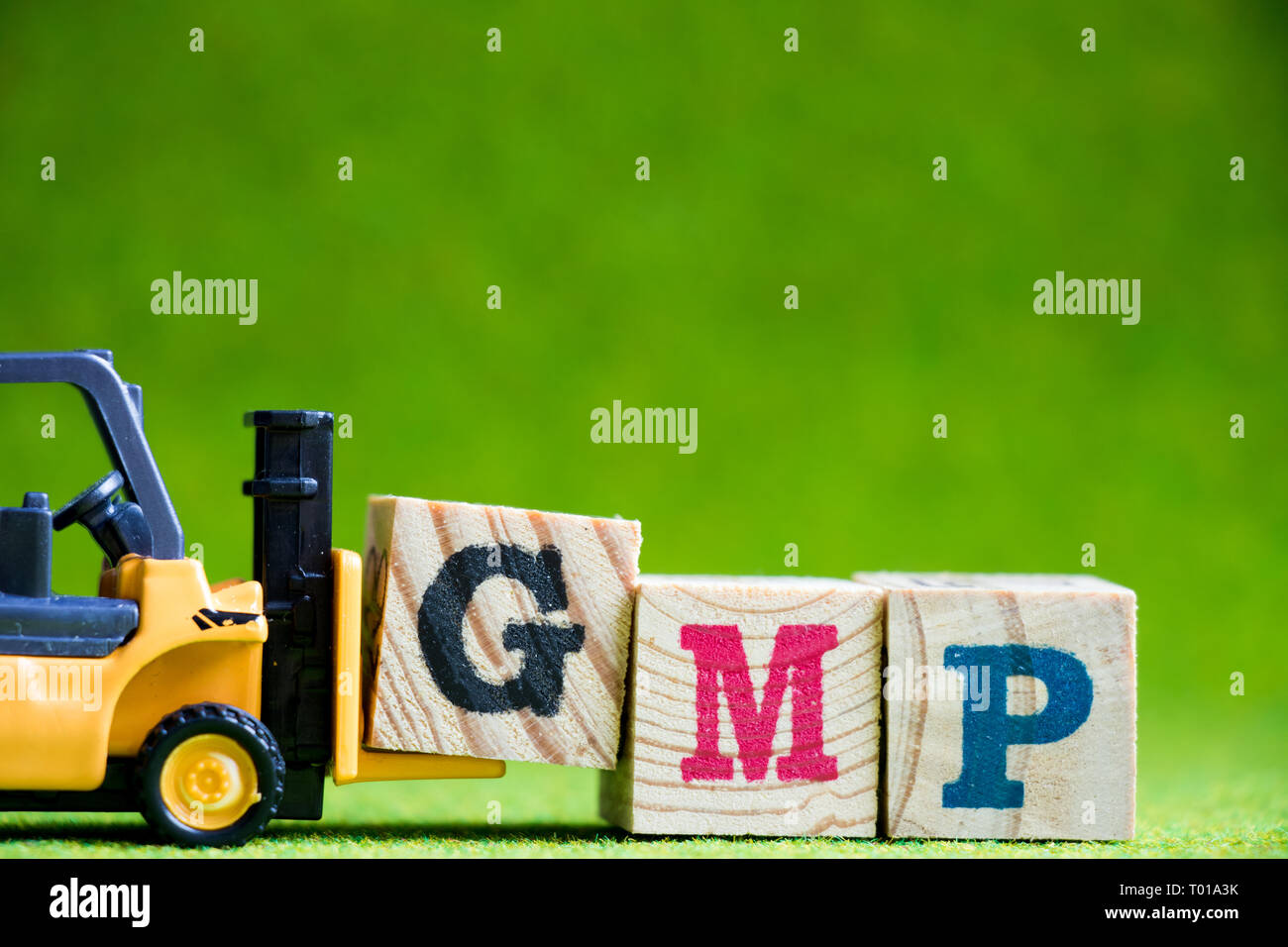 Toy forlift hold letter block G to fulfill word GMP (Abbreviation of Good Manufacturinc Practice) on green background Stock Photo