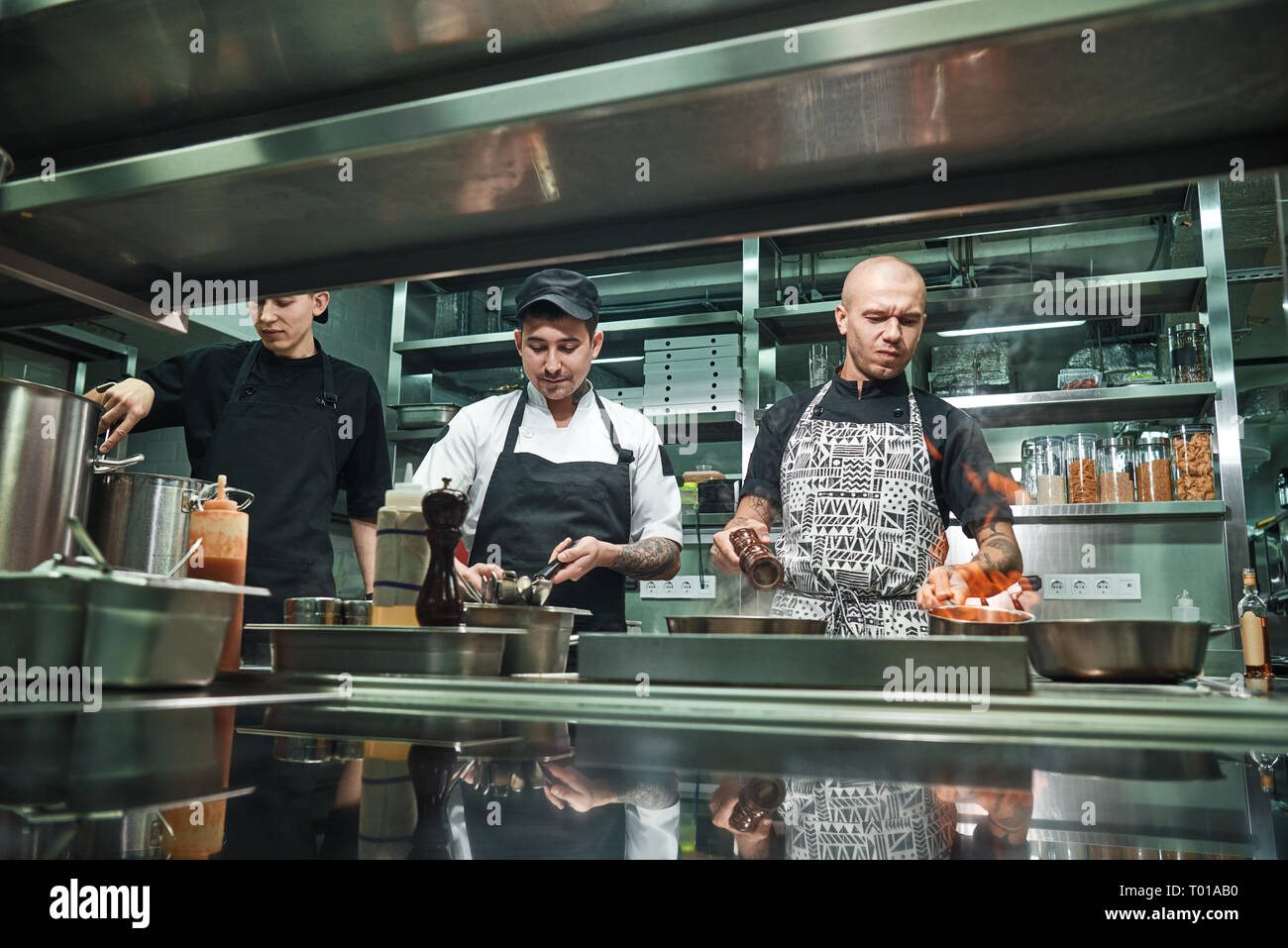 Professional team. Young brutal chef in uniform flambeing in a professional kitchen. Flambe Food Stock Photo