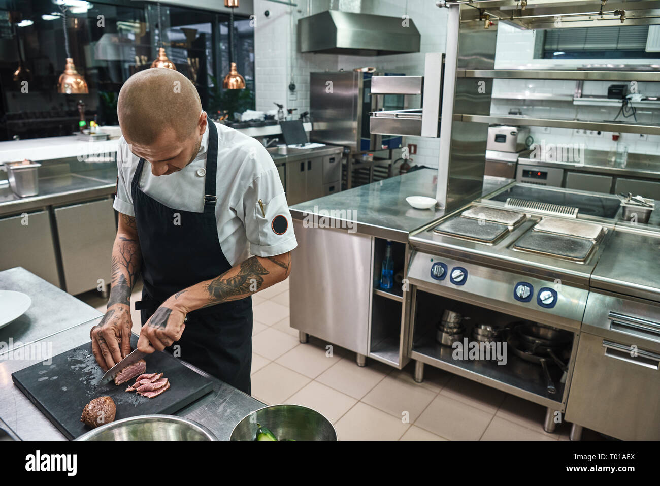 Main dish. Male bald chef with beautiful tattoos on his hands cutting a