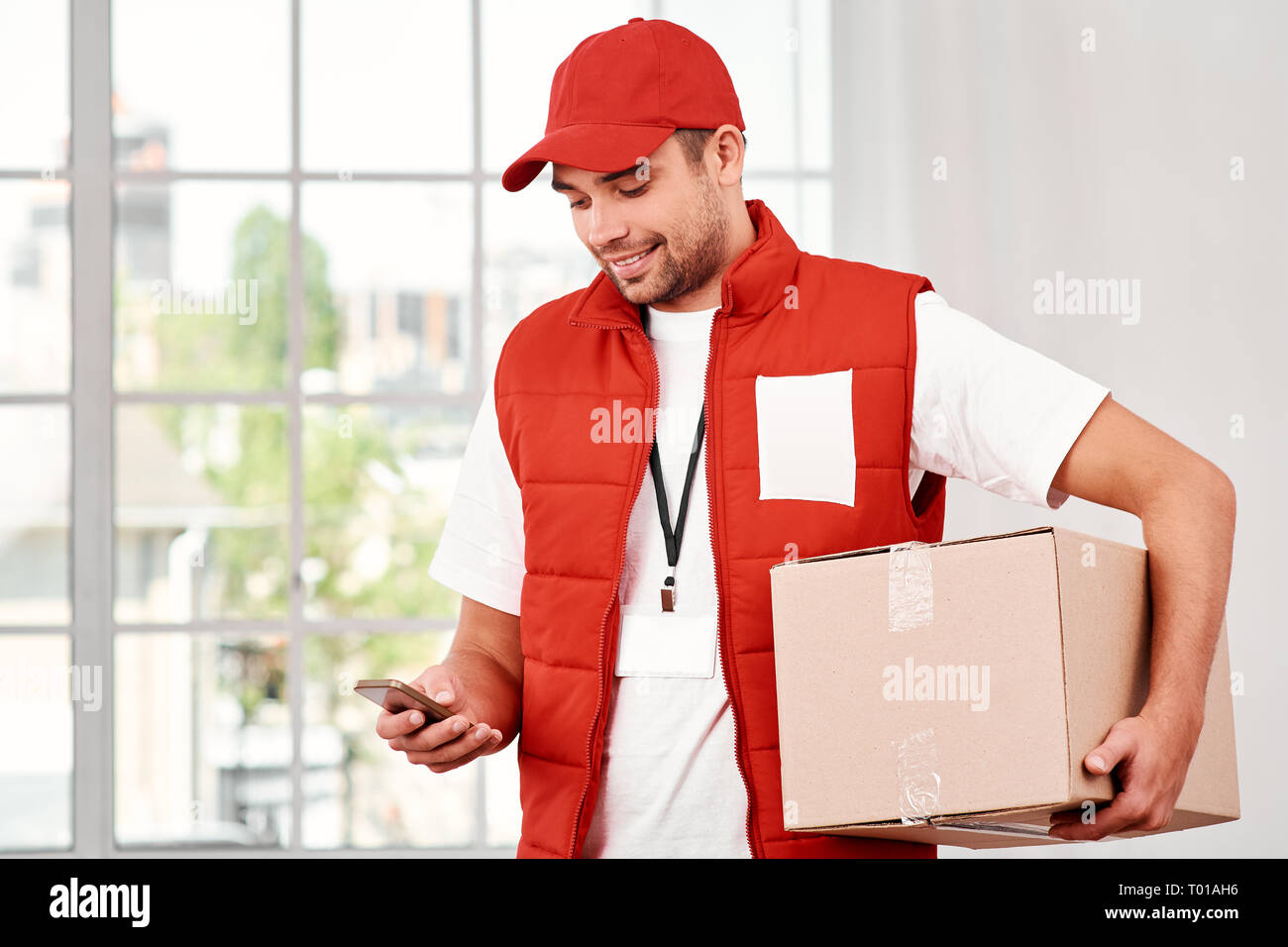 Busy postman wearing red postal uniform is delivering parcel to a
