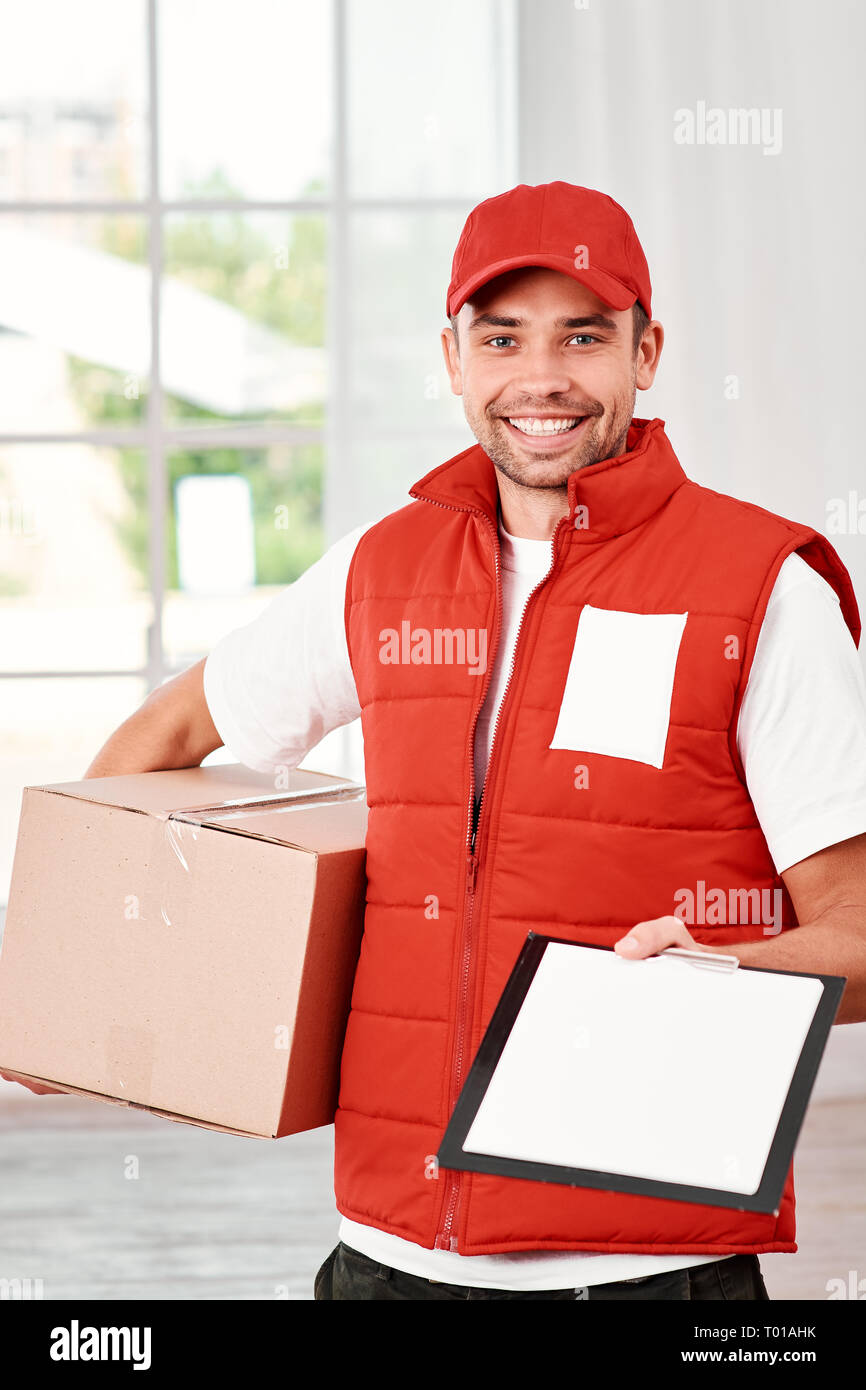Cheerful postman wearing red postal uniform is delivering parcel to a