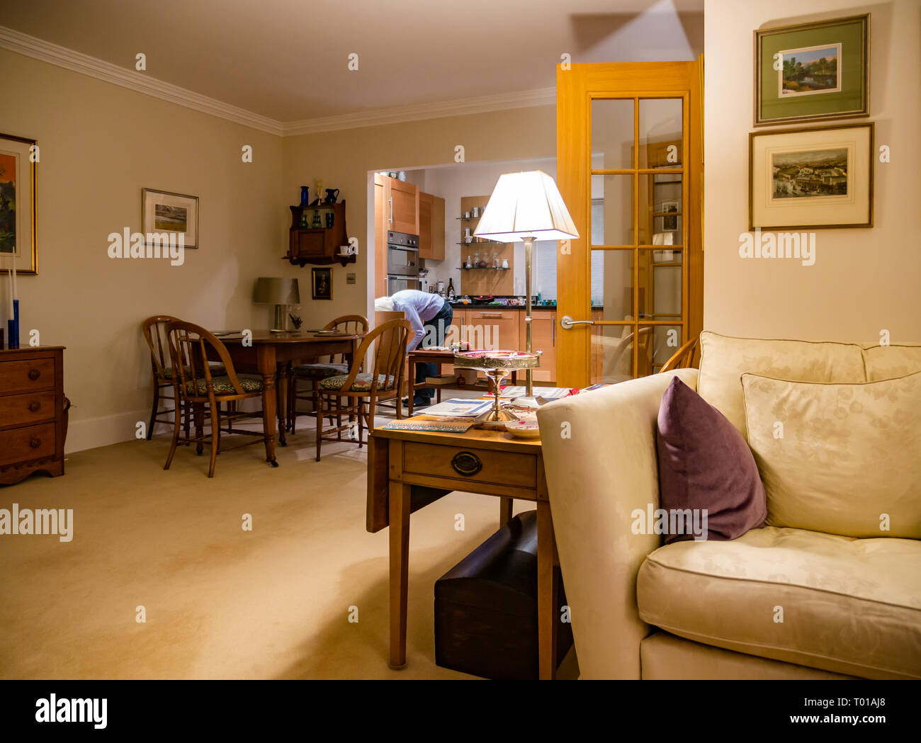 Modern open plan home interior with sitting room, dining table and kitchen with antique furniture, London, England, UK. Senior woman in kitchen Stock Photo