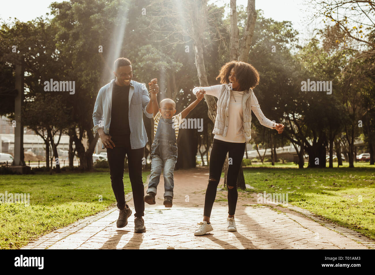 Happy beautiful family of three walking in park. Happy couple in playful mood outdoors enjoying with their child. Stock Photo