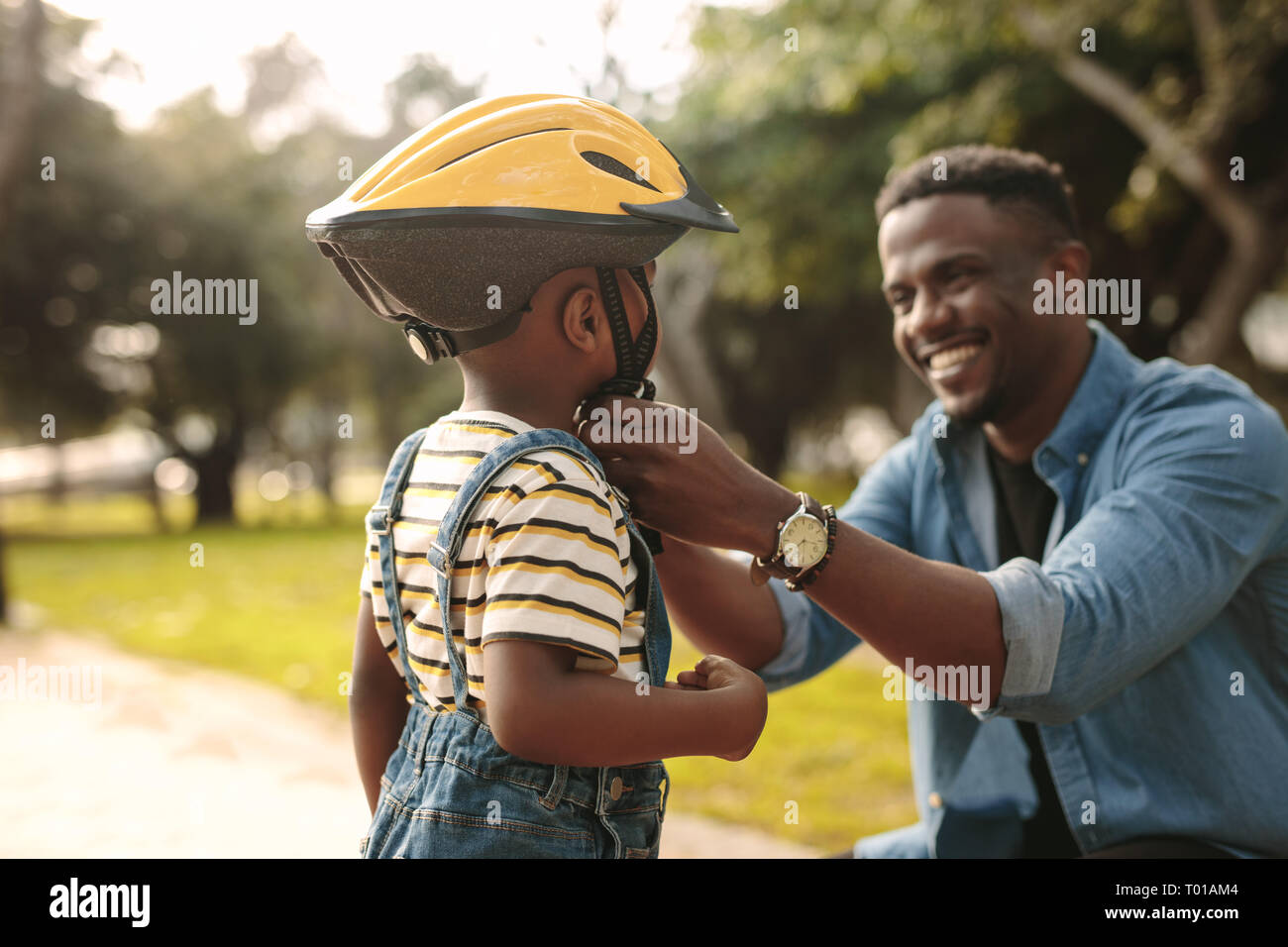 Man helps boy fastens protective helmet for learning to ride bicycle at park. Father helping his son to wear a cycling helmet. Stock Photo