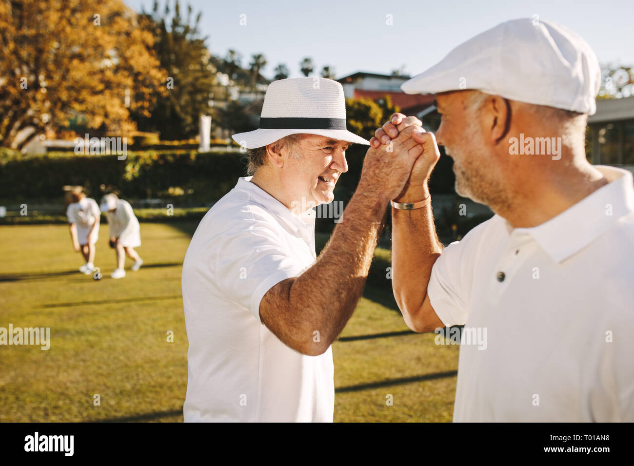 Senior men giving high five celebrating success. Elderly people enjoying a game of boules in a park. Stock Photo