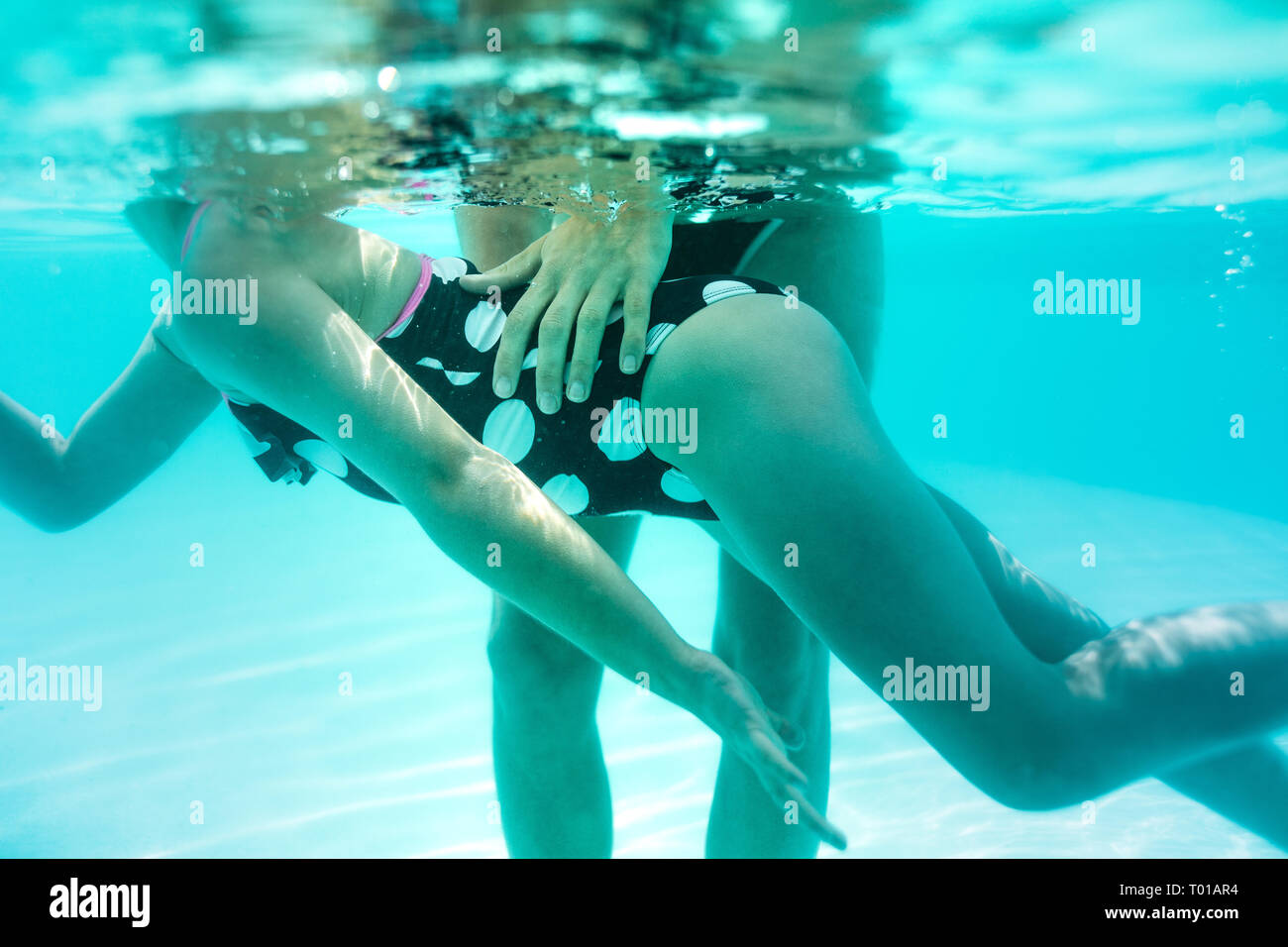 Under water shot of woman teaching his girl to swim in the pool. Girl in swimsuit learning to swim with coach at the leisure center. Stock Photo