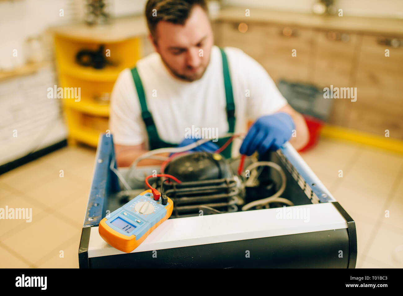 Worker in uniform testing refrigerator at home Stock Photo