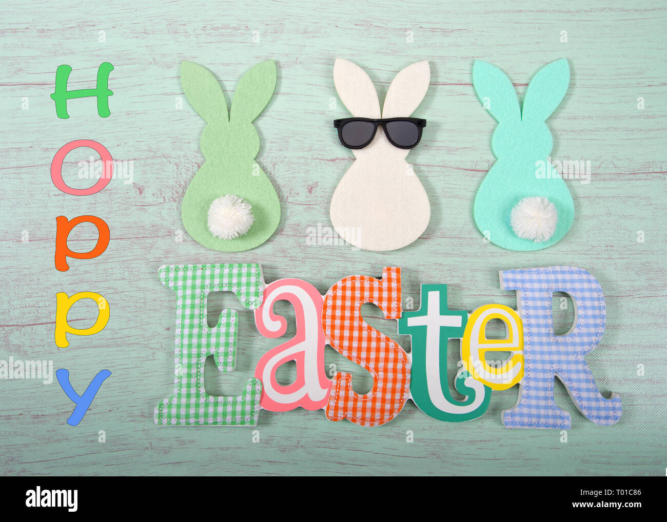 Felt bunnies in earth tone colors in a row, middle bunny wearing fun sunglasses other bunnies bottoms forward. Easter sign below. Hoppy Easter theme. Stock Photo