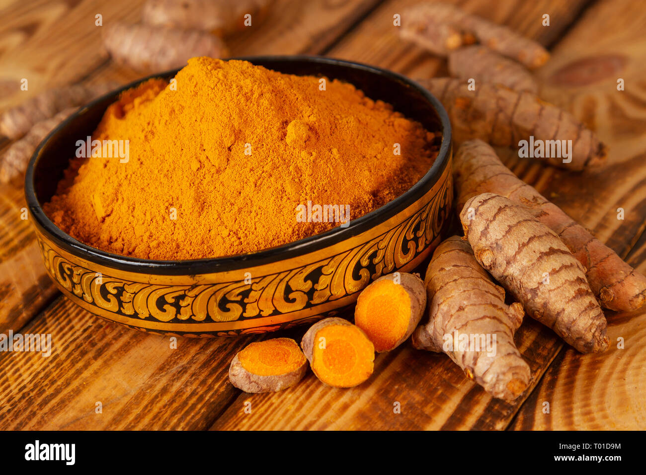 Turmeric powder in a asian bowl and turmeric roots in close up Stock Photo