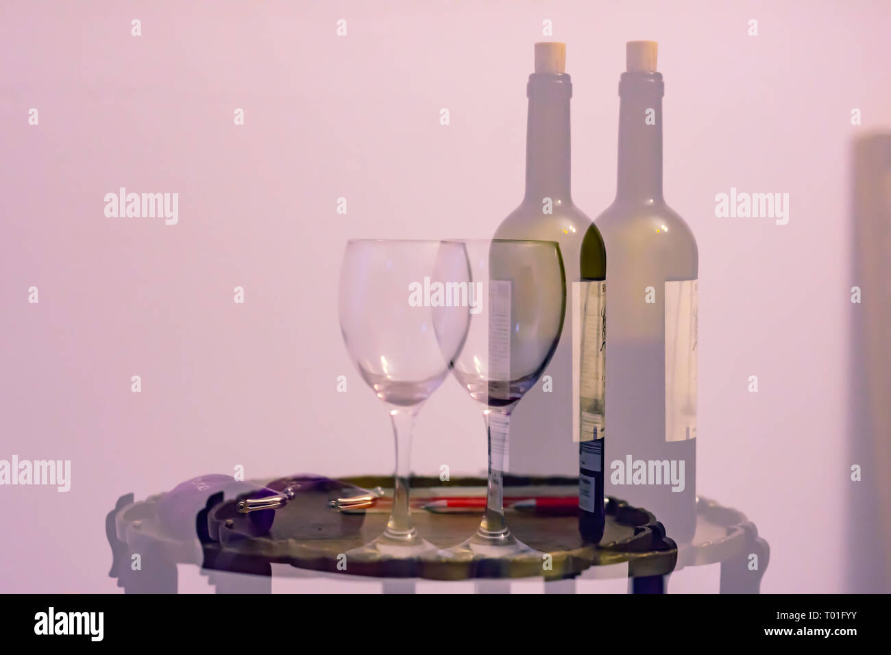 Double vision after alcohol consumption.Double exposure image of bottle of wine and empty glass placed on small tea table with purse.Costs of drinking. Stock Photo