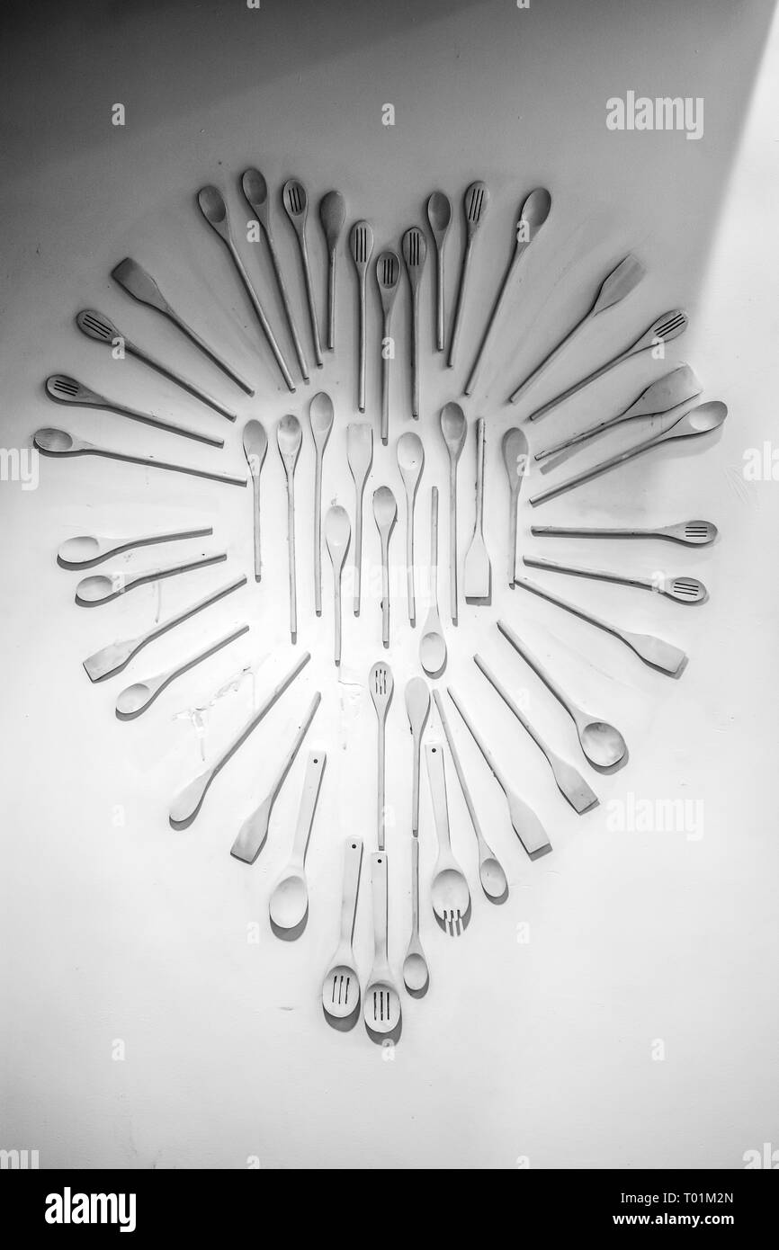 A black and white image of a wall decoration in the shape of a heart, made up of wooden kitchen utinsels. Stock Photo