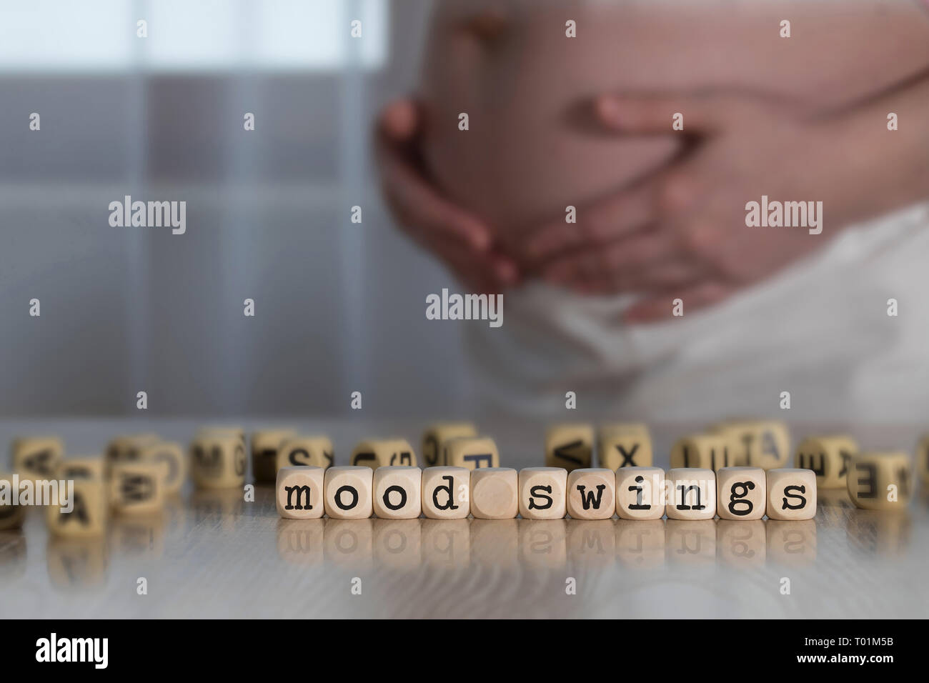 Words MOOD SWINGS  composed of wooden letters. Pregnant woman in the background Stock Photo