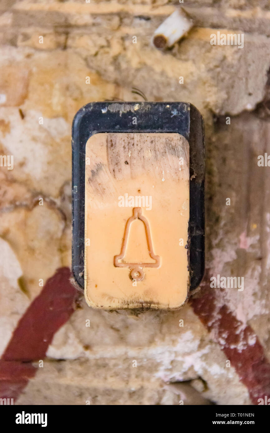 A plastic button with a flesh-colored doorphone bell with traces of damage and scratches attached to a brick wall. Push-button guest entrance outside  Stock Photo