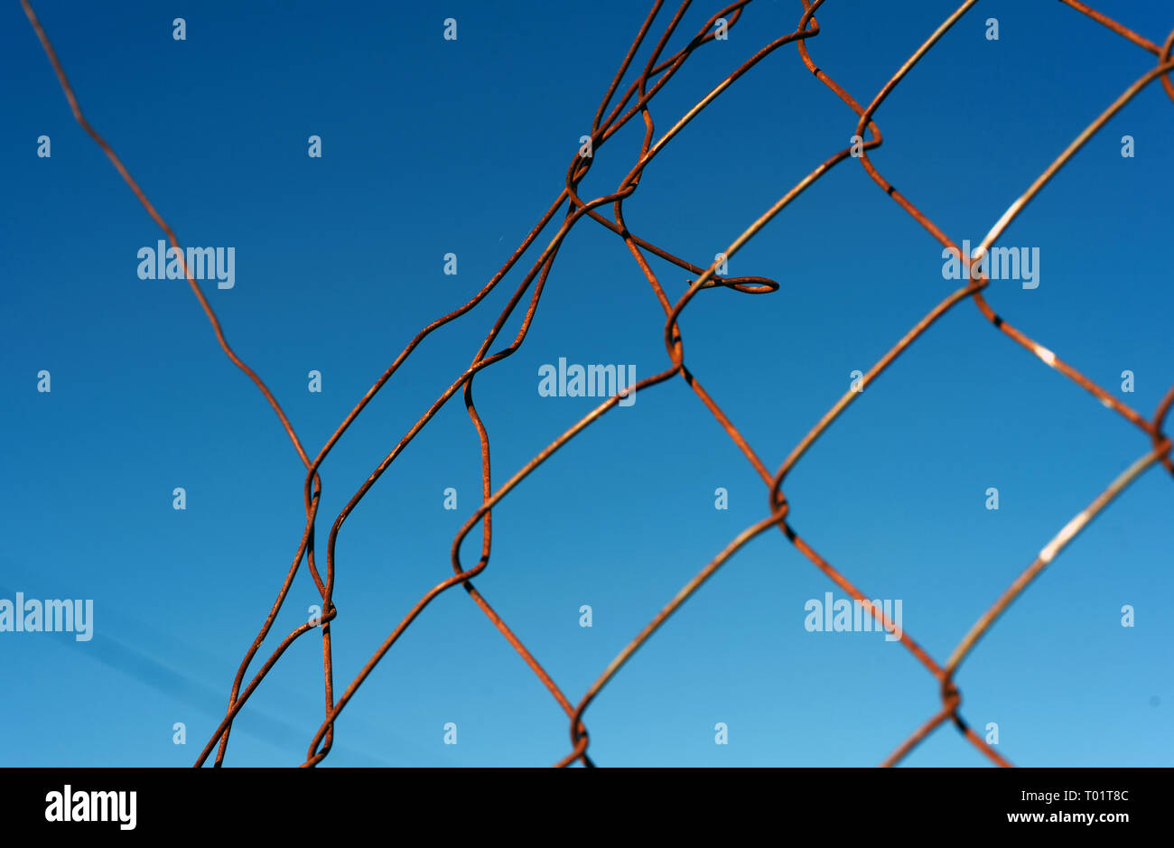 Broken and damaged chainlink mesh wire fence with a blue sky and a whole in the fencing Stock Photo