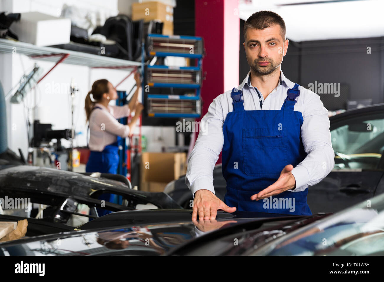 Confident mechanic demonstrating repainted car in auto repair shop Stock Photo