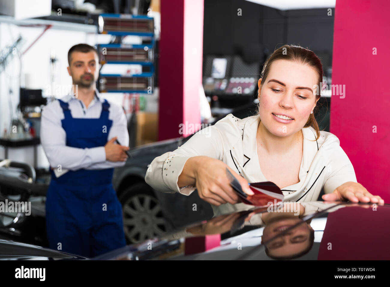 Smiling female client with paint samples choosing color for painting car at auto repair shop Stock Photo