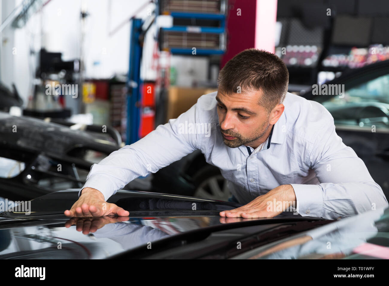 Male customer carefully examining car body after repainting in auto workshop Stock Photo