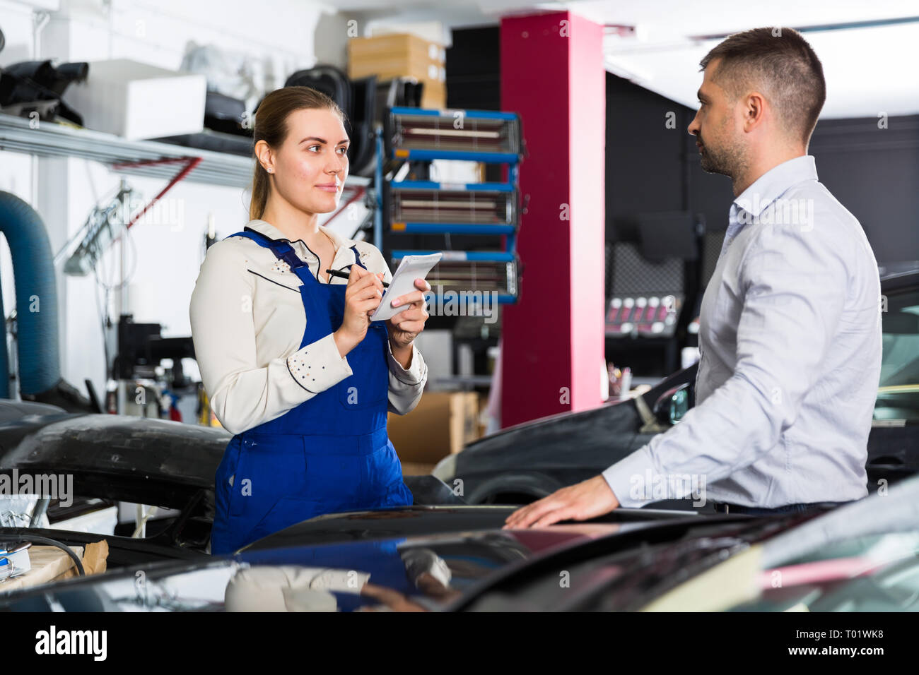 Professional female mechanic discussing with male client and recording list of works on car repair in auto repair shop Stock Photo