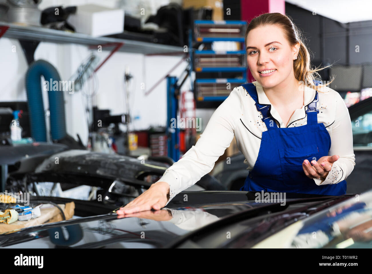 Young woman mechanic demonstrating repainted car in auto repair shop Stock Photo