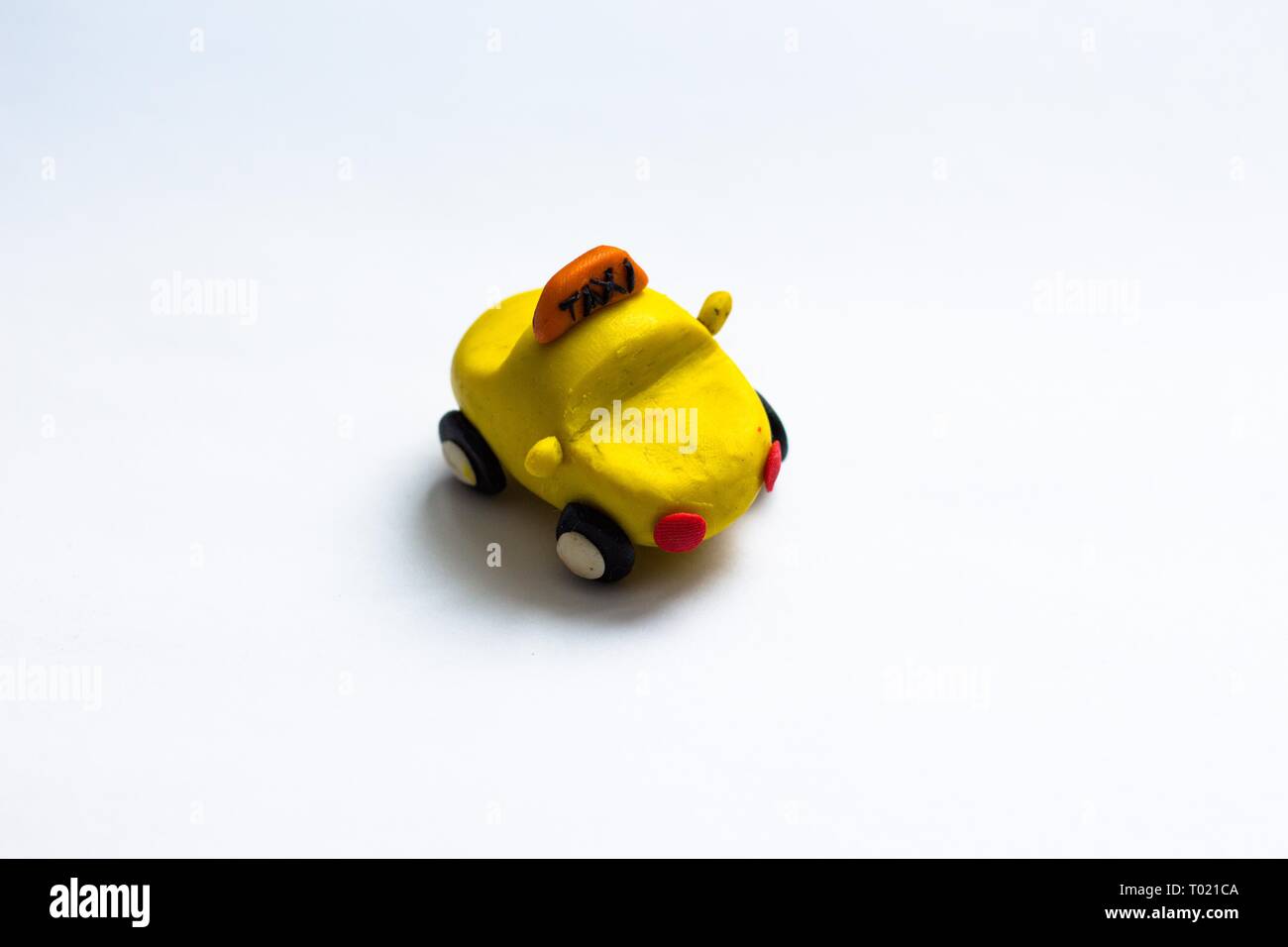 A small yellow cab made of plasticine stands on a white background. The car wheels are black and red headlights. Stock Photo