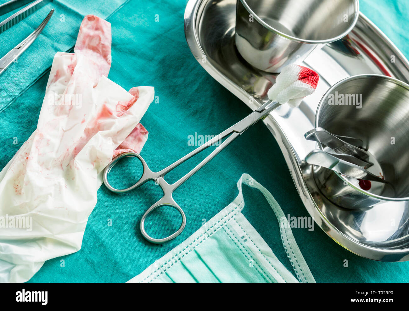 Scene details of operating theater after surgical operation, gloves spotted with blood along container tweezers and scissors of suture, conceptual ima Stock Photo