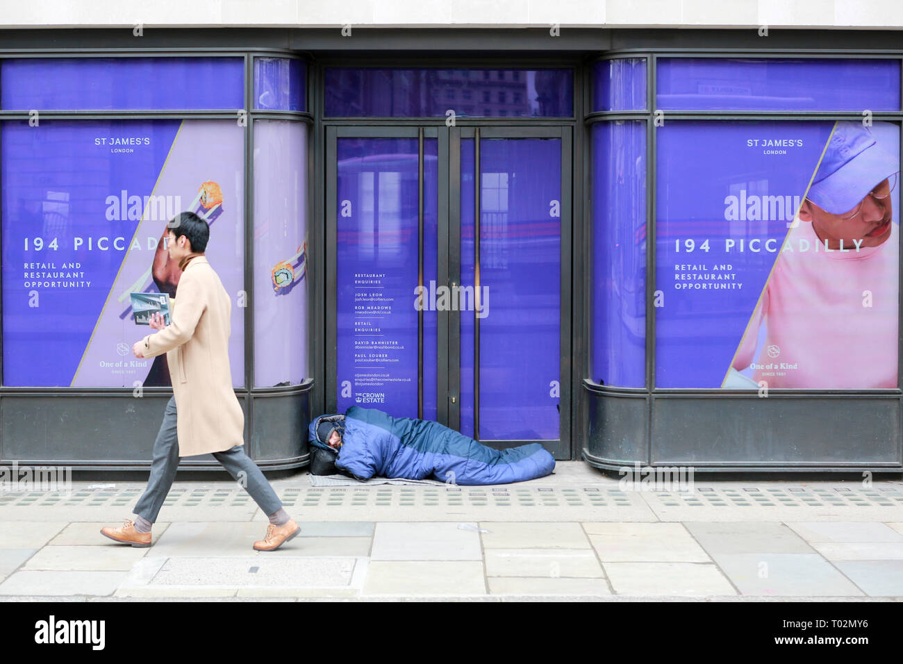 London, UK. 16th March, 2019. A man walks past a homeless man asleep on Piccadilly. Penelope Barritt/Alamy Live news Stock Photo