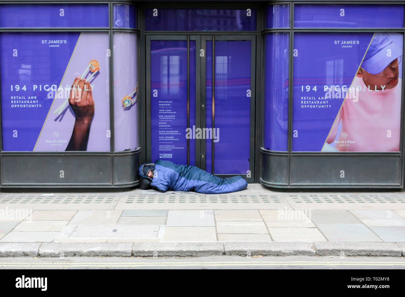 London, UK. 16th March, 2019. A man walks past a homeless man asleep on Piccadilly. Penelope Barritt/Alamy Live news Stock Photo