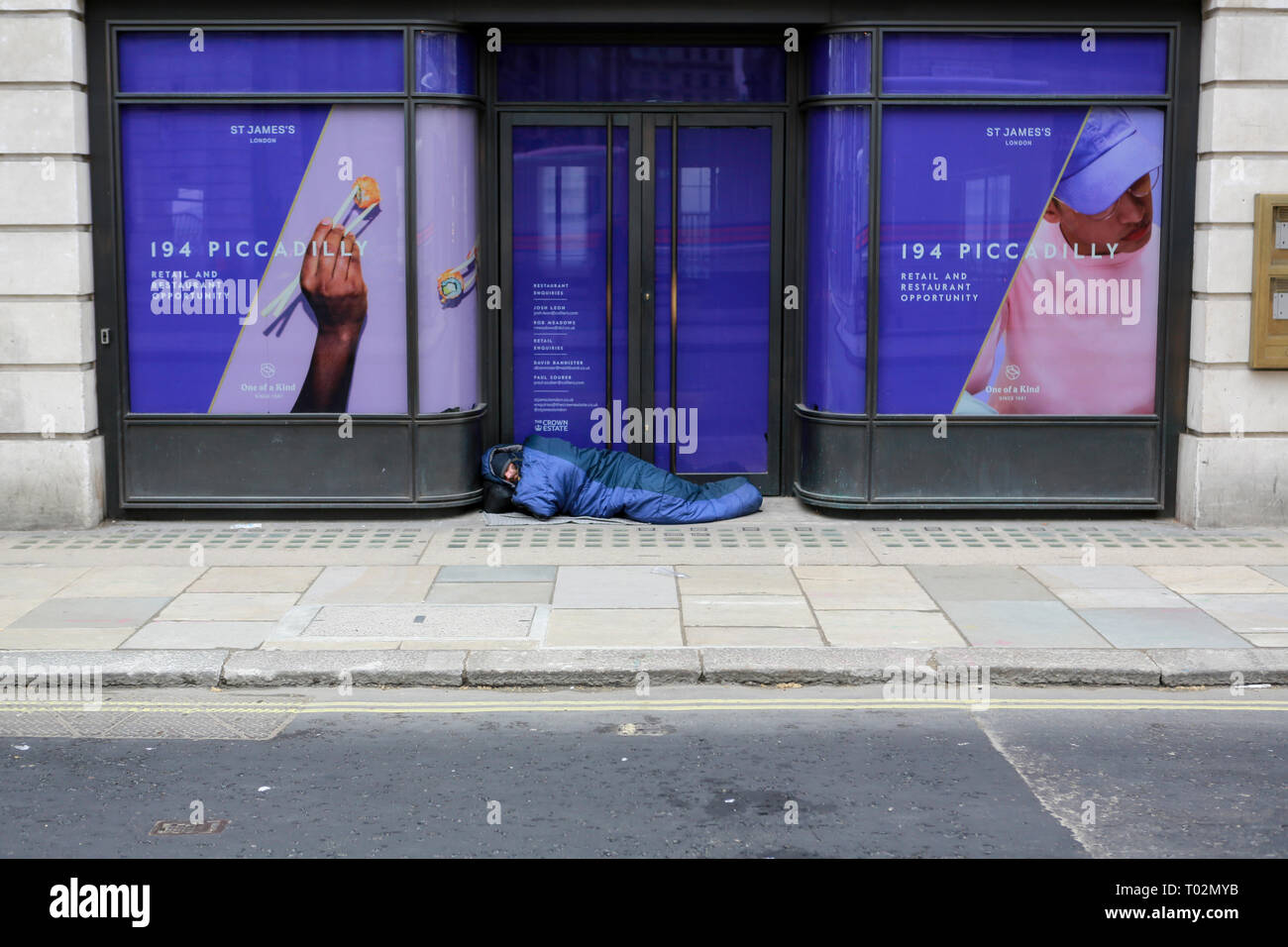 London, UK. 16th March, 2019. A man walks past a homeless man asleep on Piccadilly. Penelope Barritt/Alamy Live news Stock Photo