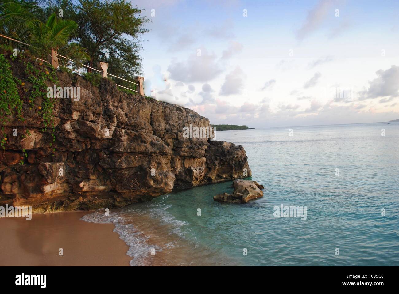 Rocky cliff walls of Taga Beach with the beautiful cove below, boasting of clear waters and soft white sand Stock Photo