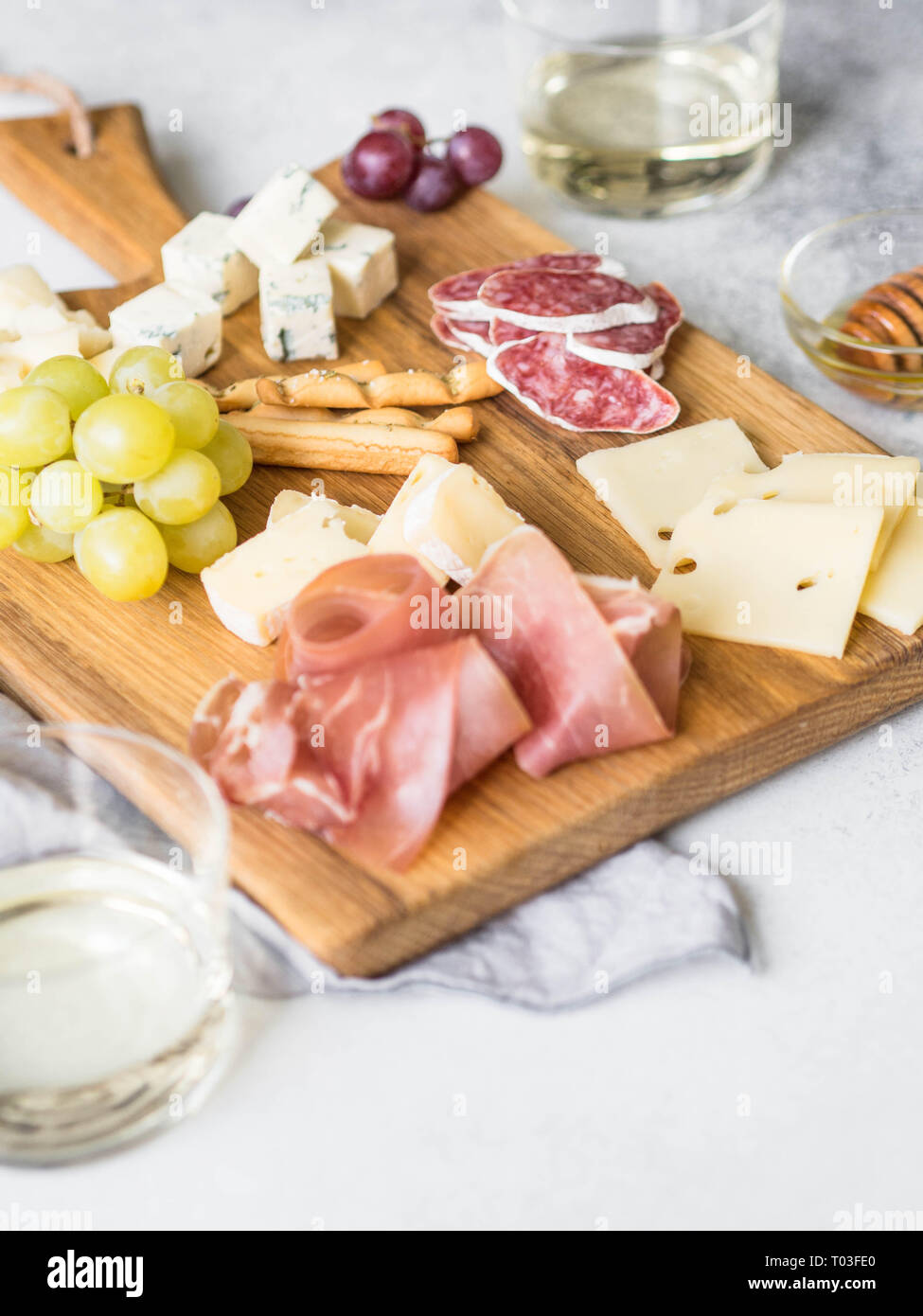 Cheese and meat wine snack set on wood board . Variety of cheese, salami, prosciutto, bread sticks, honey, grapes and two glasses with wine. Stock Photo