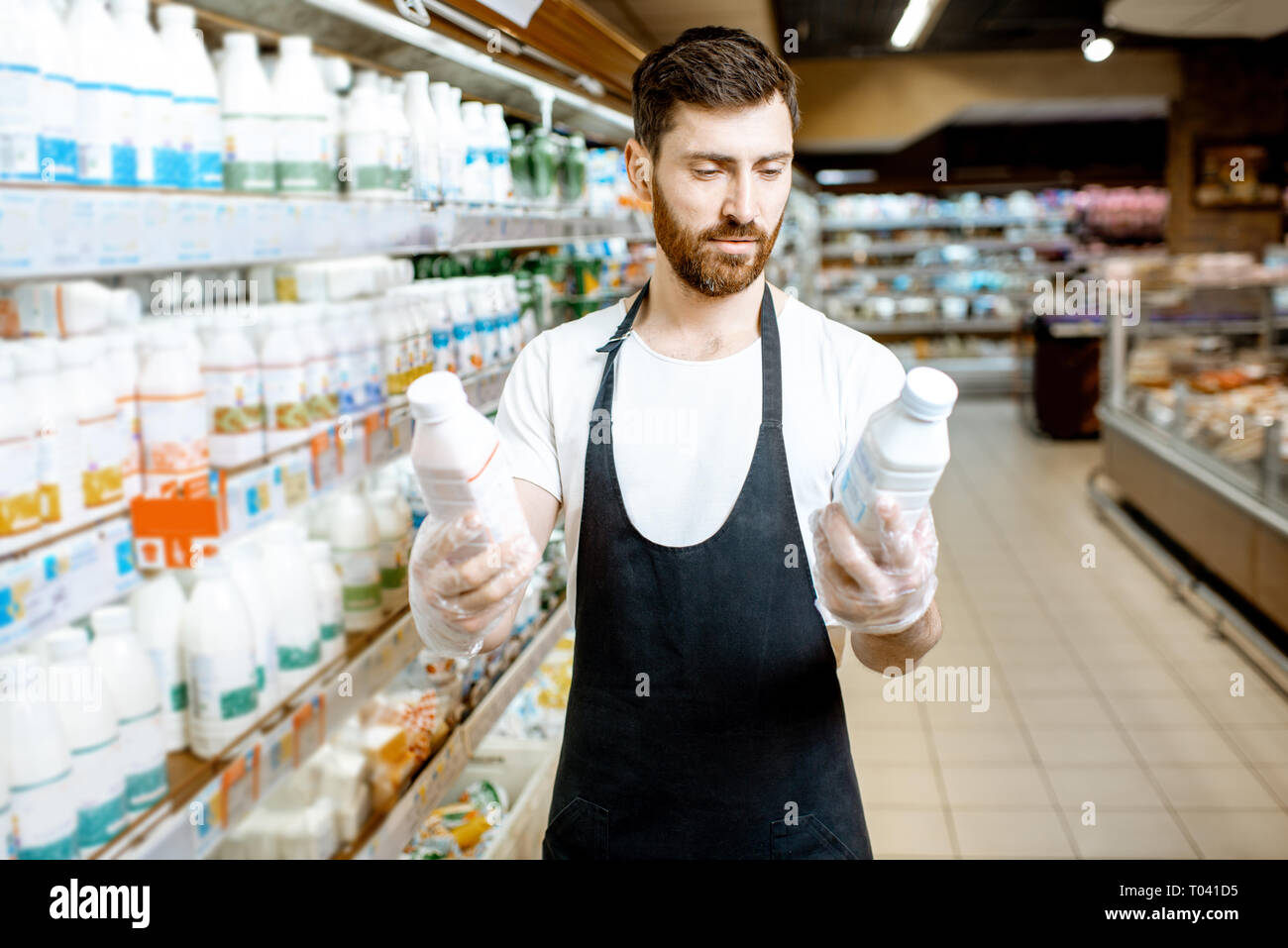 Shop worker looking on the bottles with milk standing near the shelves with dairy products in the supermarket Stock Photo