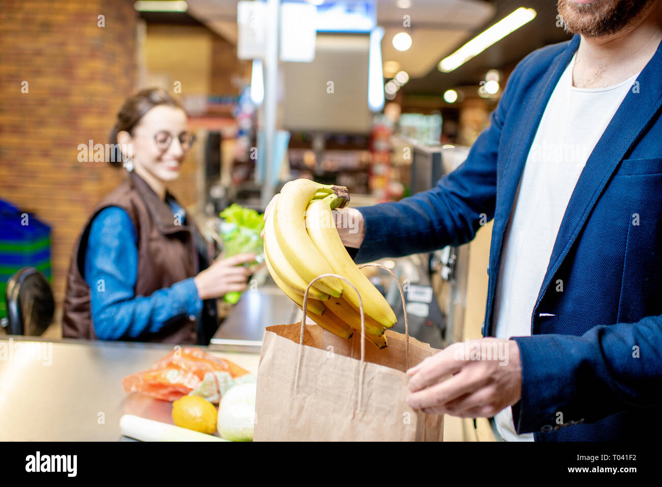 Businessman buying healthy food, packing products at the cash register with cashier on the background, close-up view Stock Photo