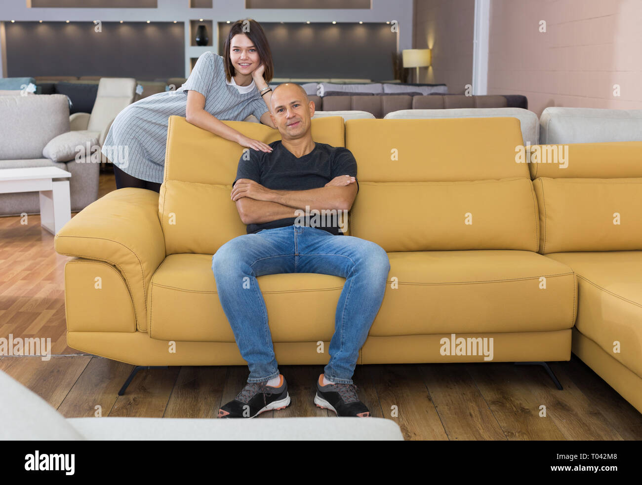 Happy Husband And Wife Sitting On Bright Yellow Couch In Furniture