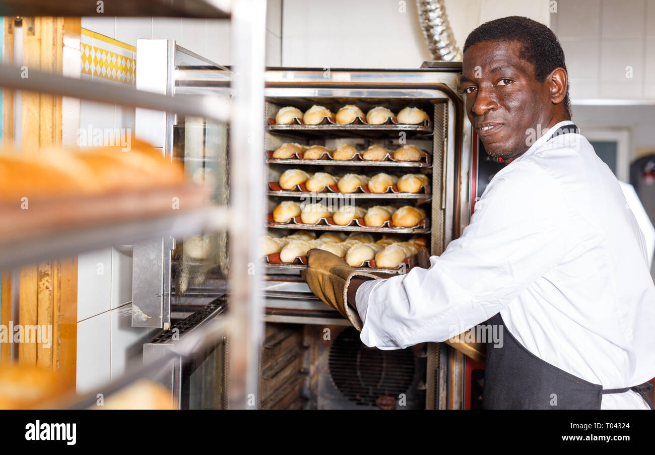 Experienced baker working in small bakery, taking out bread from industrial oven Stock Photo